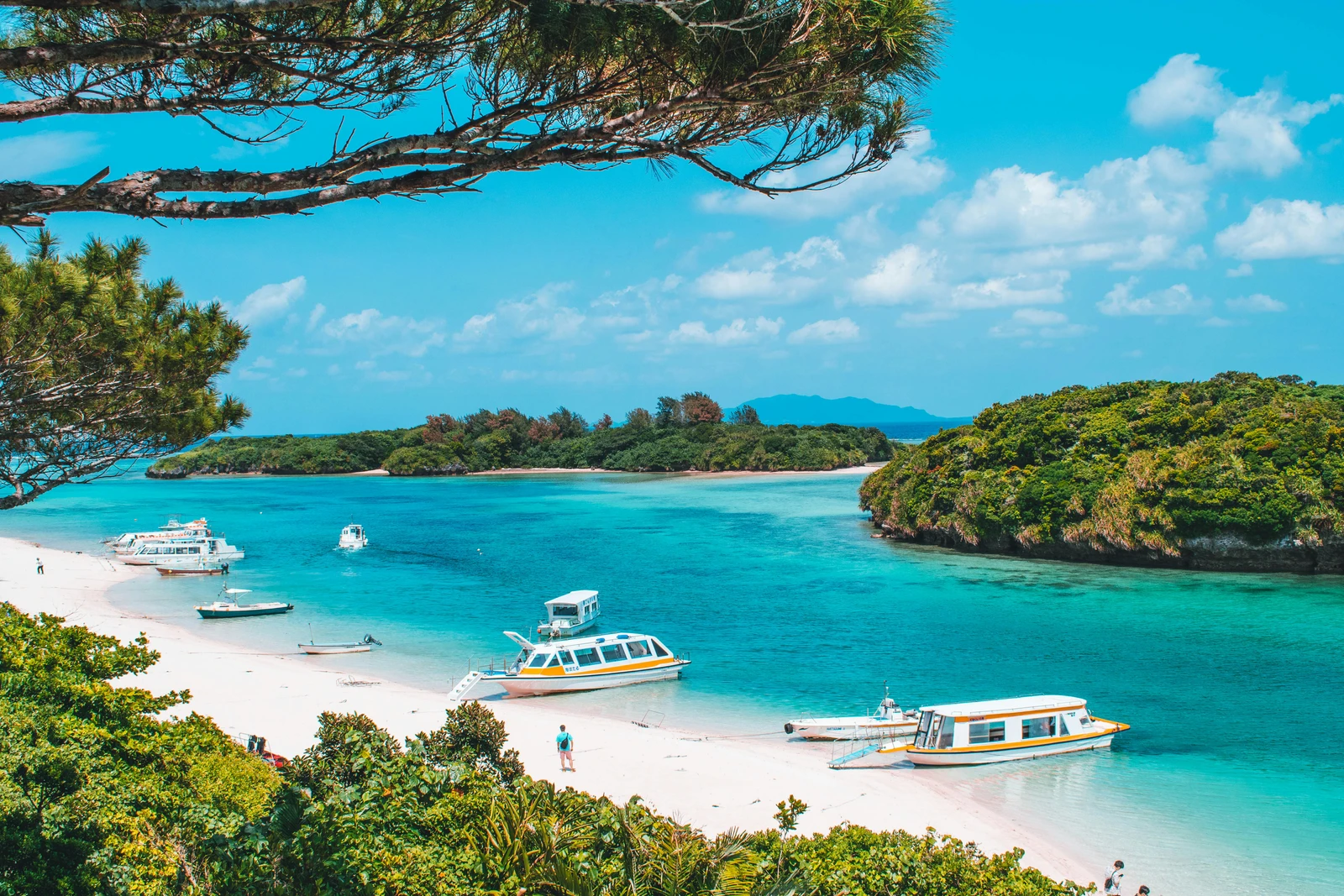 Turquoise lagoon dotted with tour boats along a forested bay in Japan's Okinawa Prefecture