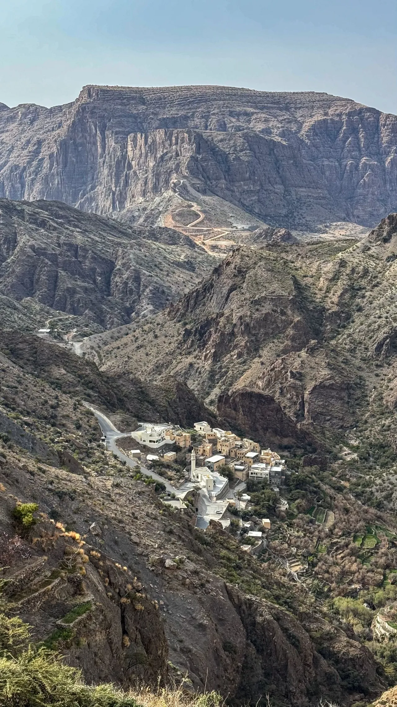 Mountain village nestled in a deep canyon on Jebel Akhdar with switchback roads carved into the cliff face above