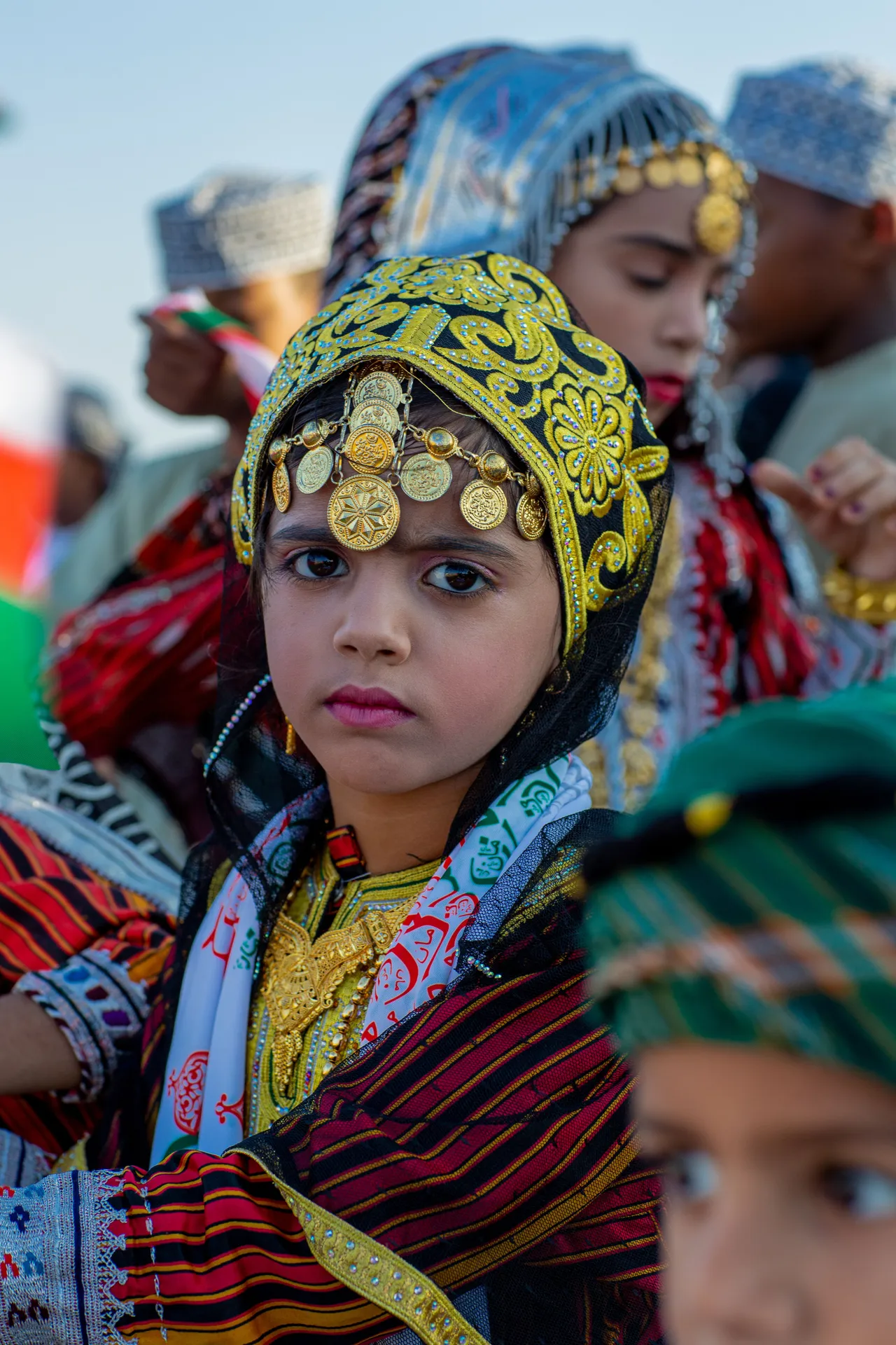 Young Omani girl in traditional gold-embroidered headdress and colourful dress at a national celebration in Muscat