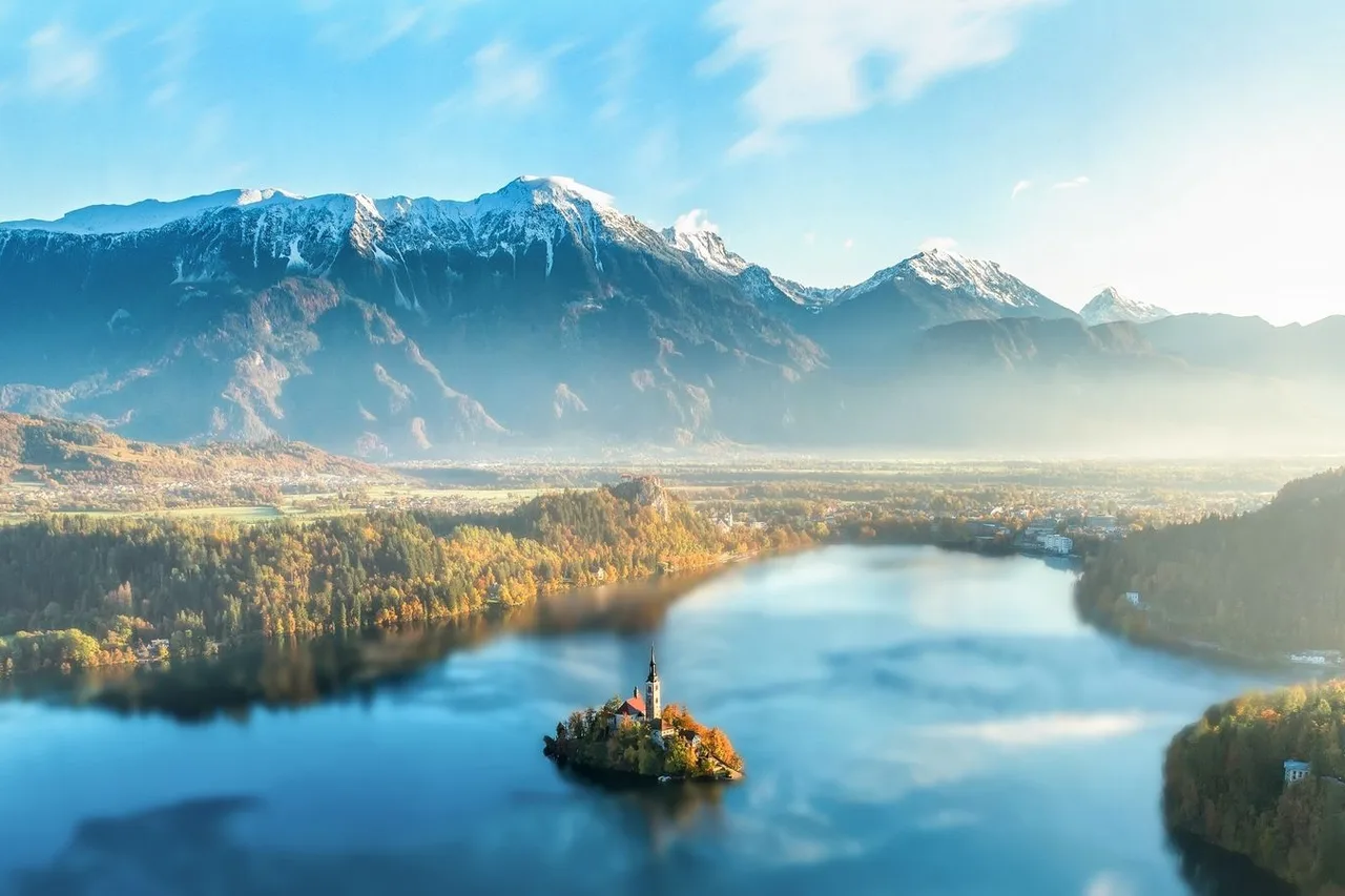 Aerial view of Lake Bled with its island church and Bled Castle, framed by the snow-capped Julian Alps