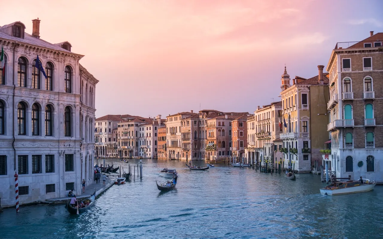 Grand Canal in Venice at sunset with gondolas and Renaissance palazzo facades in warm pink light