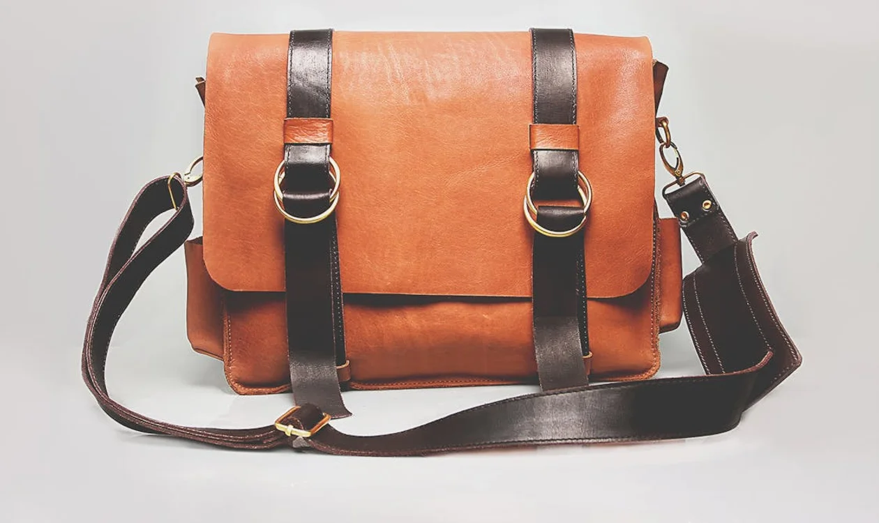 A leather and canvas weekend travel bag photographed on a hotel bench beside a folded jacket