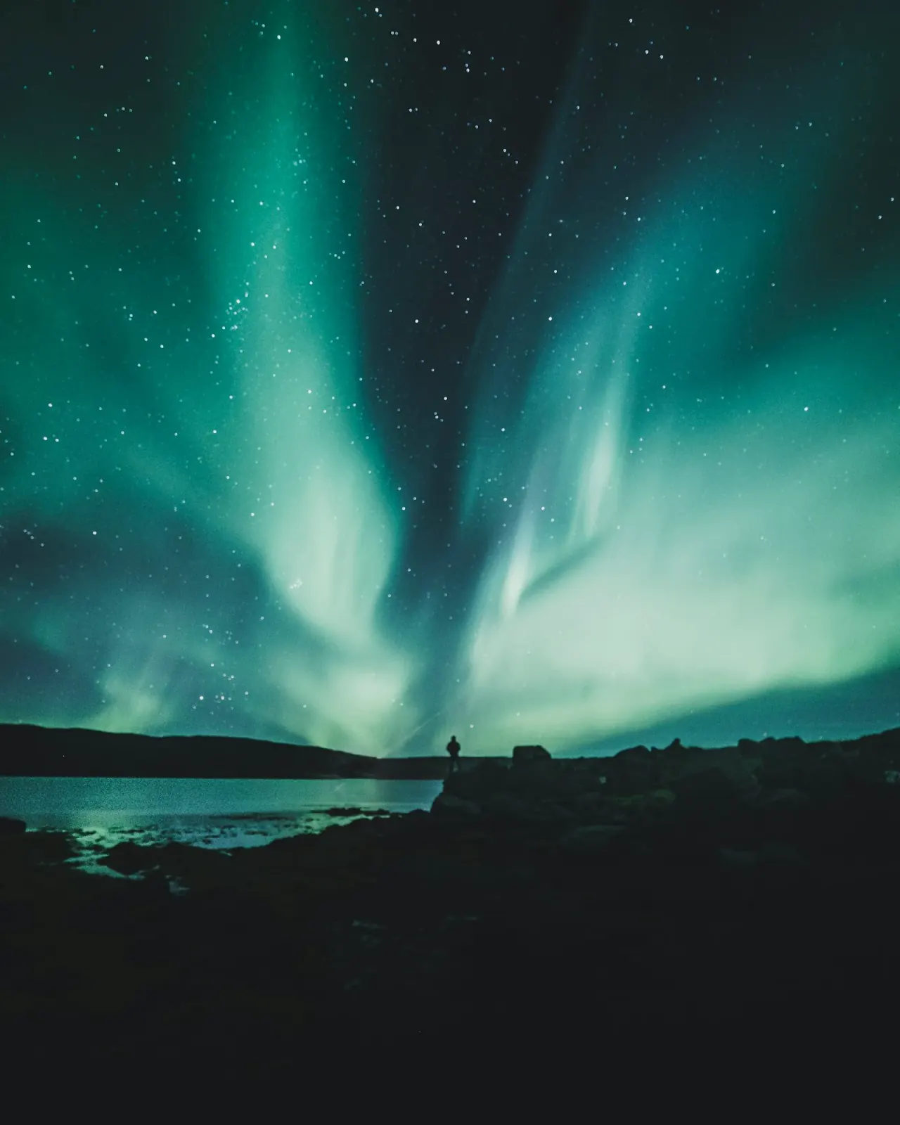 Aurora borealis arcing across an Icelandic winter sky over a snow-covered landscape